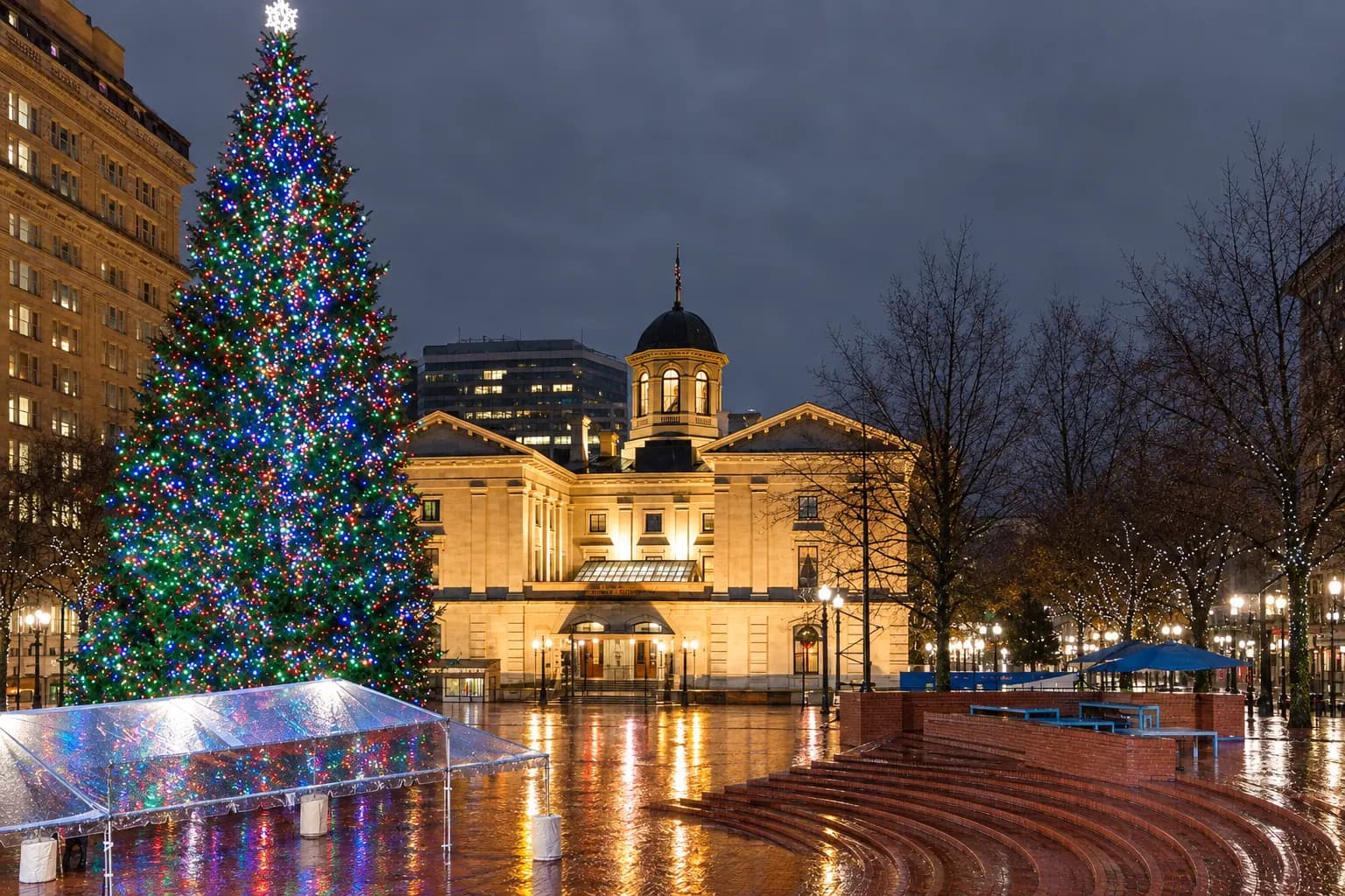 The lit Christmas tree in Pioneer Courthouse Square on a wet December evening, with Pioneer Courthouse behind it and the brick steps reflecting the lights