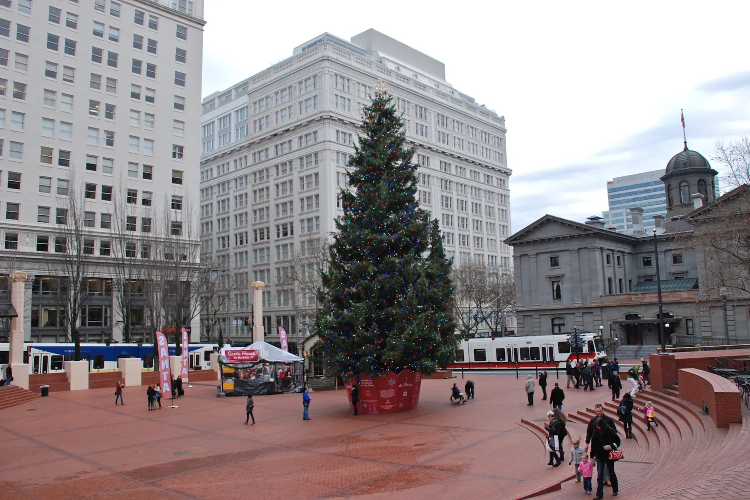 The holiday tree standing in the brick amphitheater of Pioneer Courthouse Square in downtown Portland on a gray December day, with the Pioneer Courthouse at right