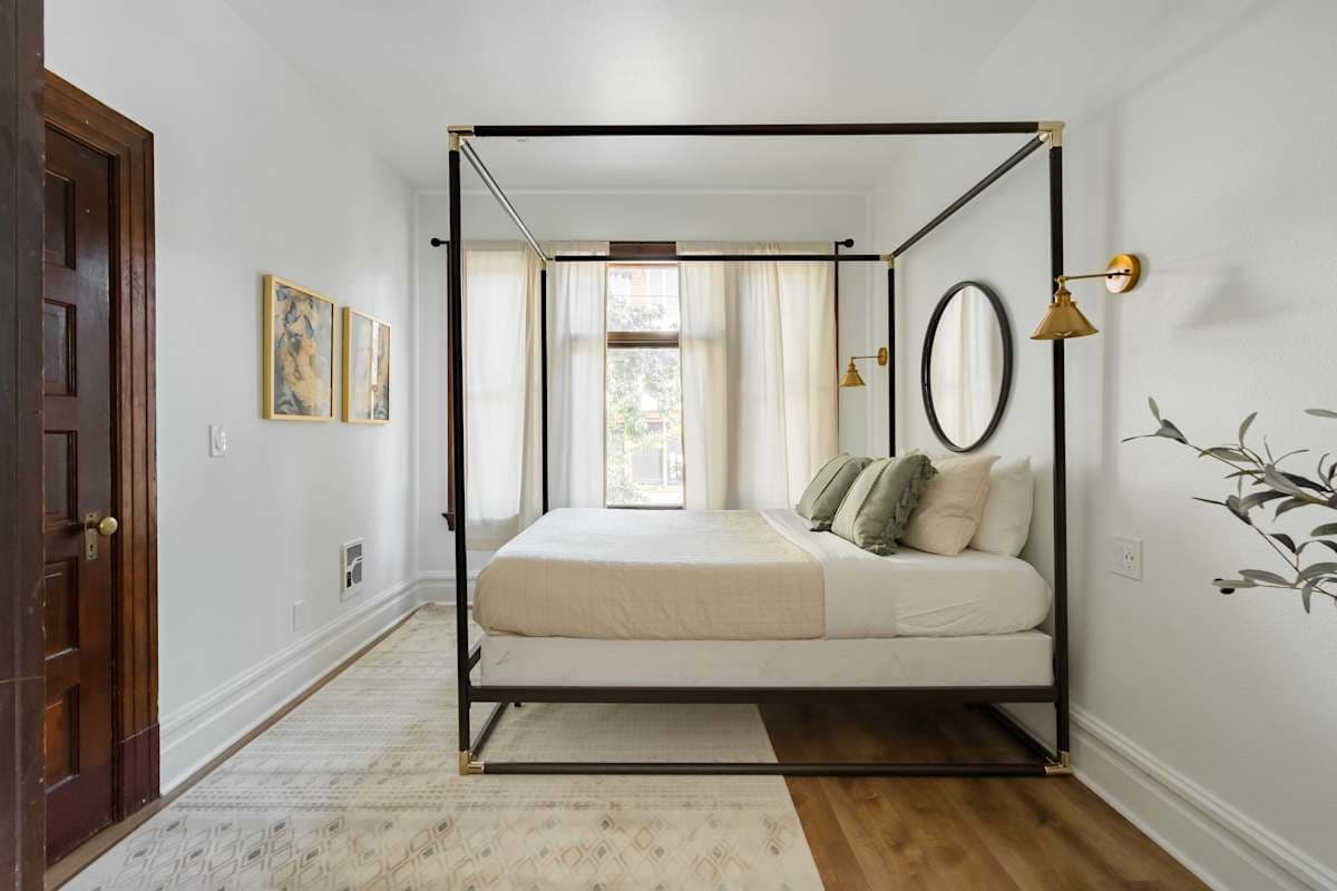 An elegant apartment bedroom with canopy bed, gold sconces, and natural light in Portland